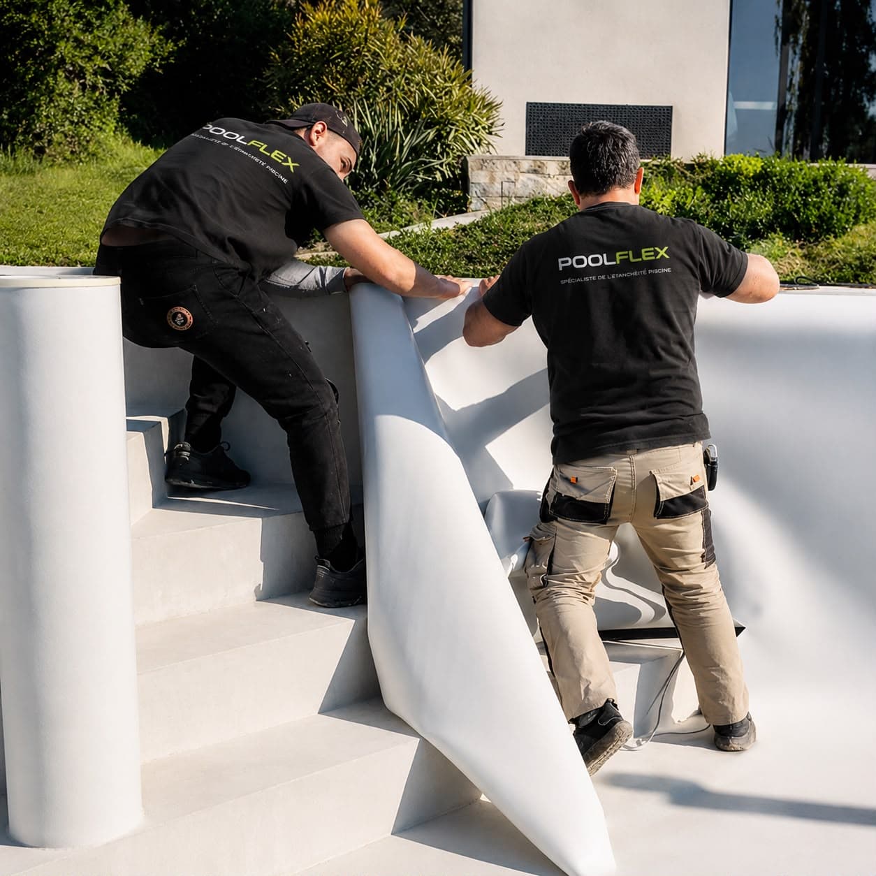 Deux poseurs Poolflex ajustent une membrane armée blanche sur les marches d’un bassin en chantier