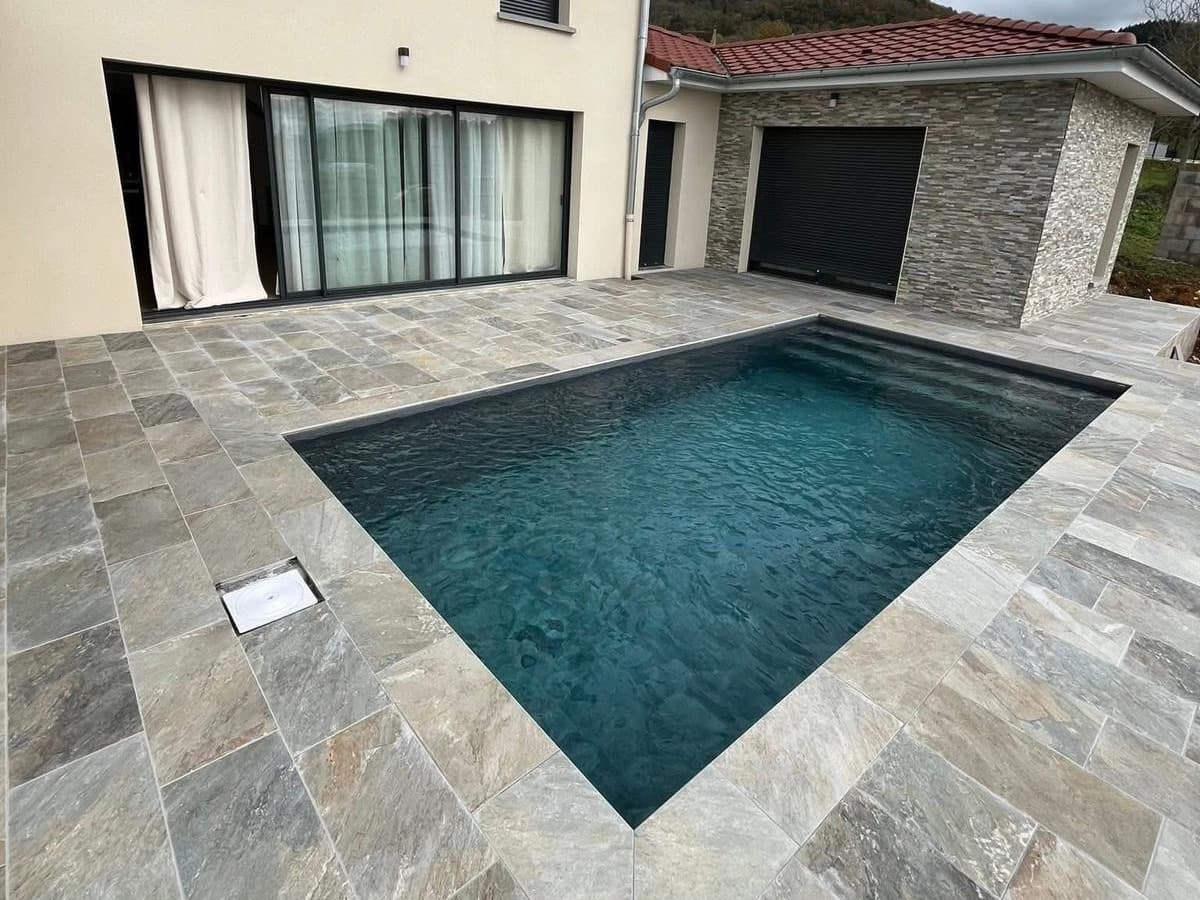 Piscine 7×3 m terminée avec liner armé gris foncé et terrasse en pierre naturelle devant une villa neuve