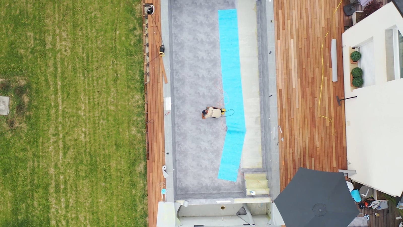 Vue aérienne du chantier : un technicien déroule les lés de membrane armée dans le bassin en construction
